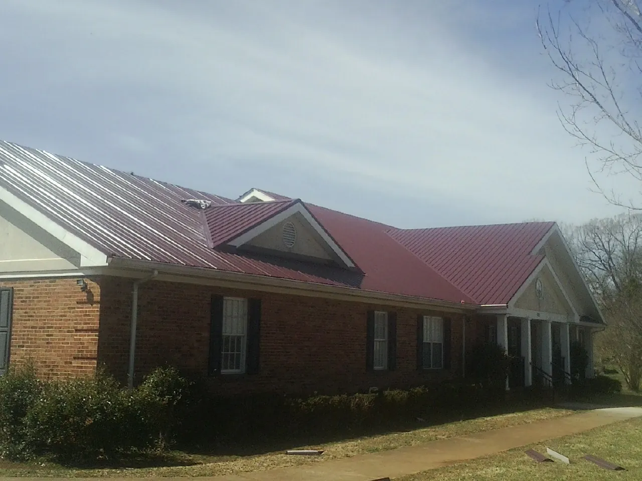 Red metal roof with gabled entries on a long brick building, from a Hail Damage Roof Repair job in Stanford