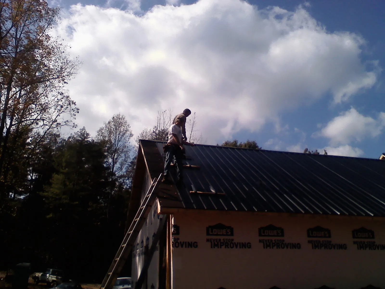 Roofer fastening dark metal panels high against a cloudy sky, from a Roof Inspection job in Stanford