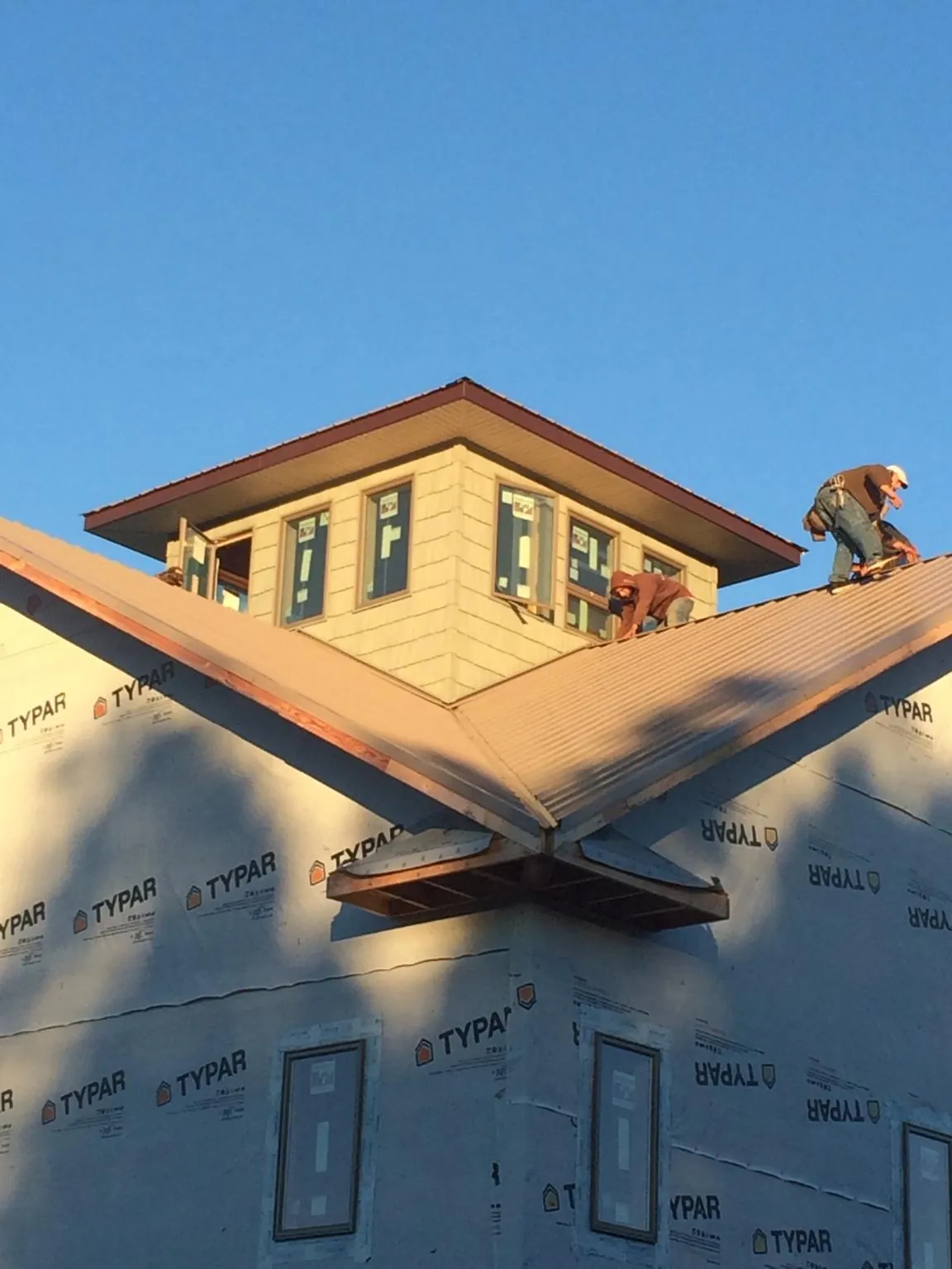 Roofers working around a rooftop cupola on a new metal roof at sunset — Roof Waterproofing in Stanford by Roofing Brothers